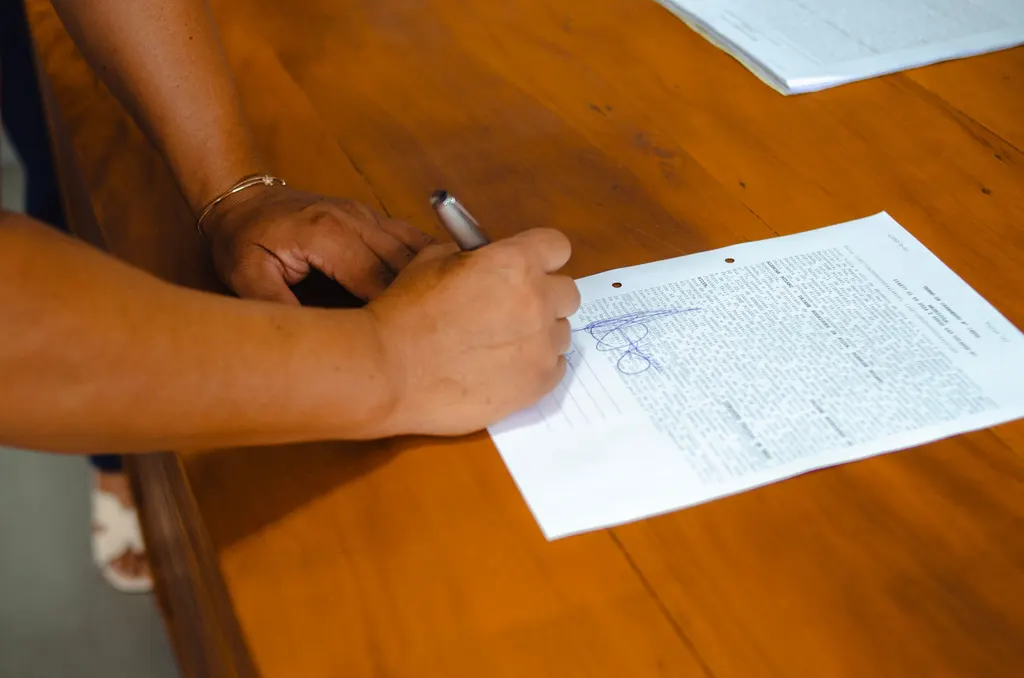 Hands signing a one-page agreement at a wooden table.
