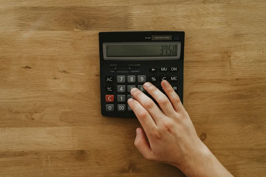 A hand on a calculator on a warm oak table.