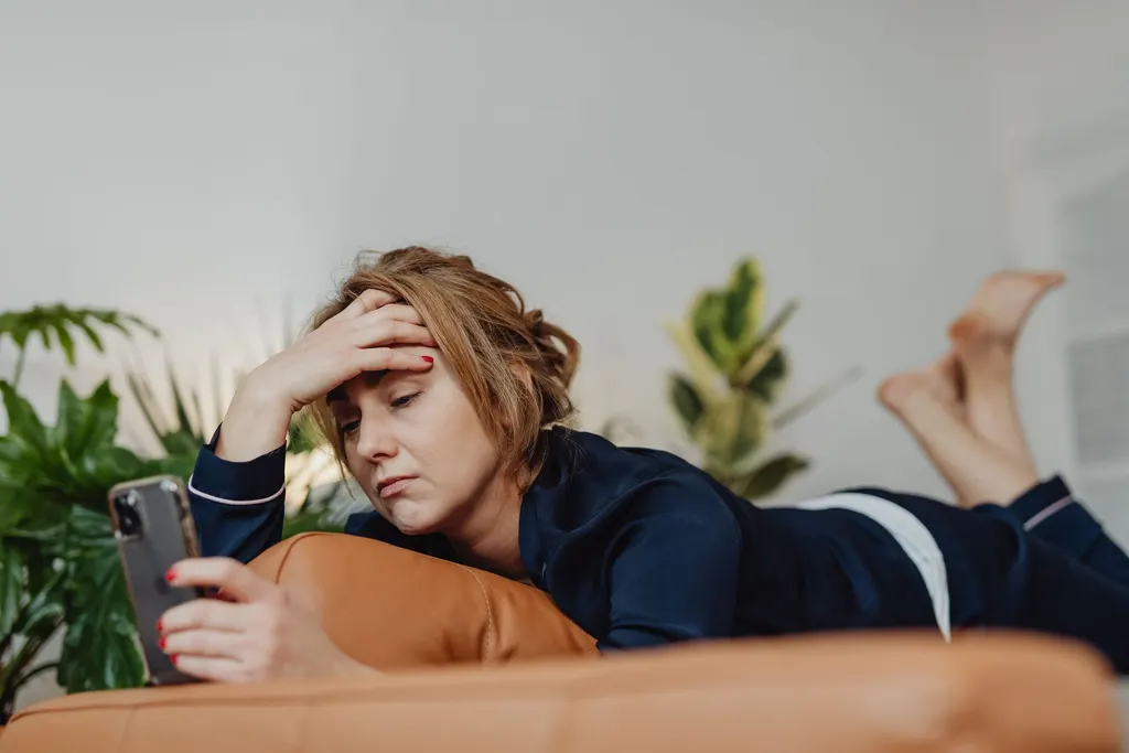 A woman lying on the sofa frowns at a message on her phone.