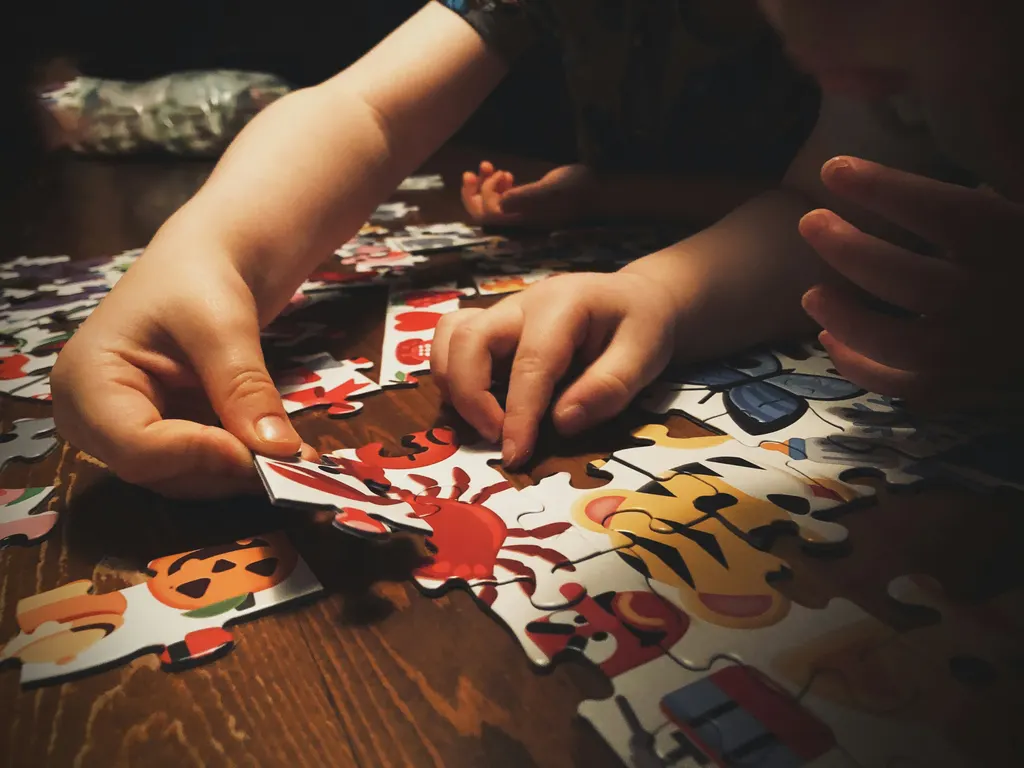 A child's hands fit pieces into a colorful jigsaw puzzle beside an adult's hand.