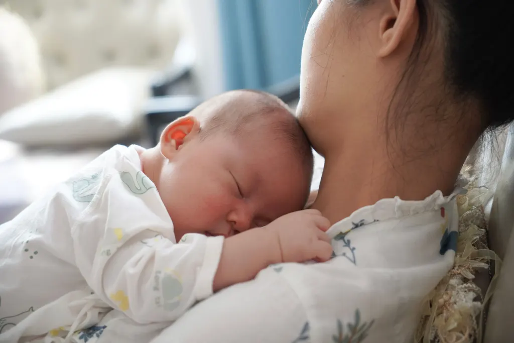 A newborn sleeps against a woman's shoulder.