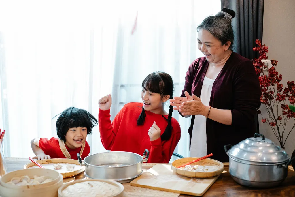 A woman and two children laugh as they make dumplings together at the kitchen table.