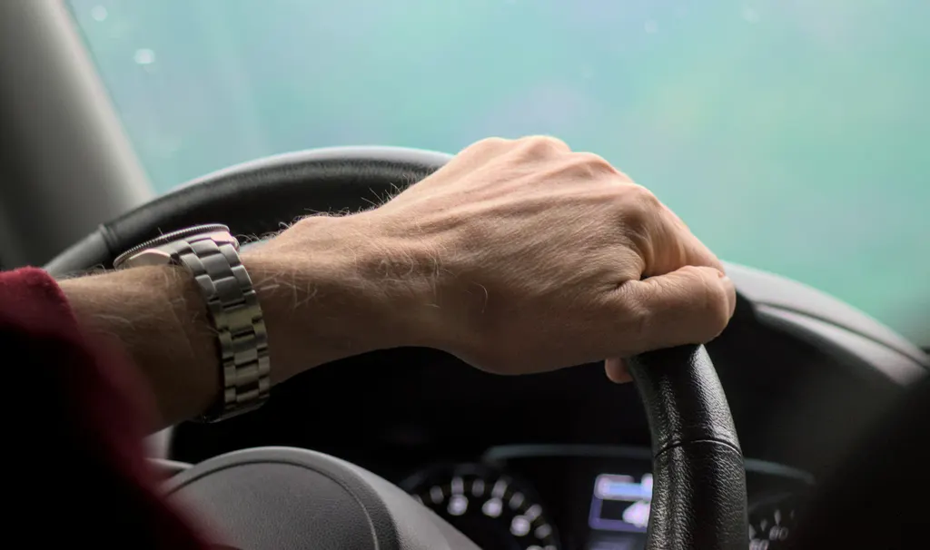 A driver's hand on the steering wheel of a moving car.