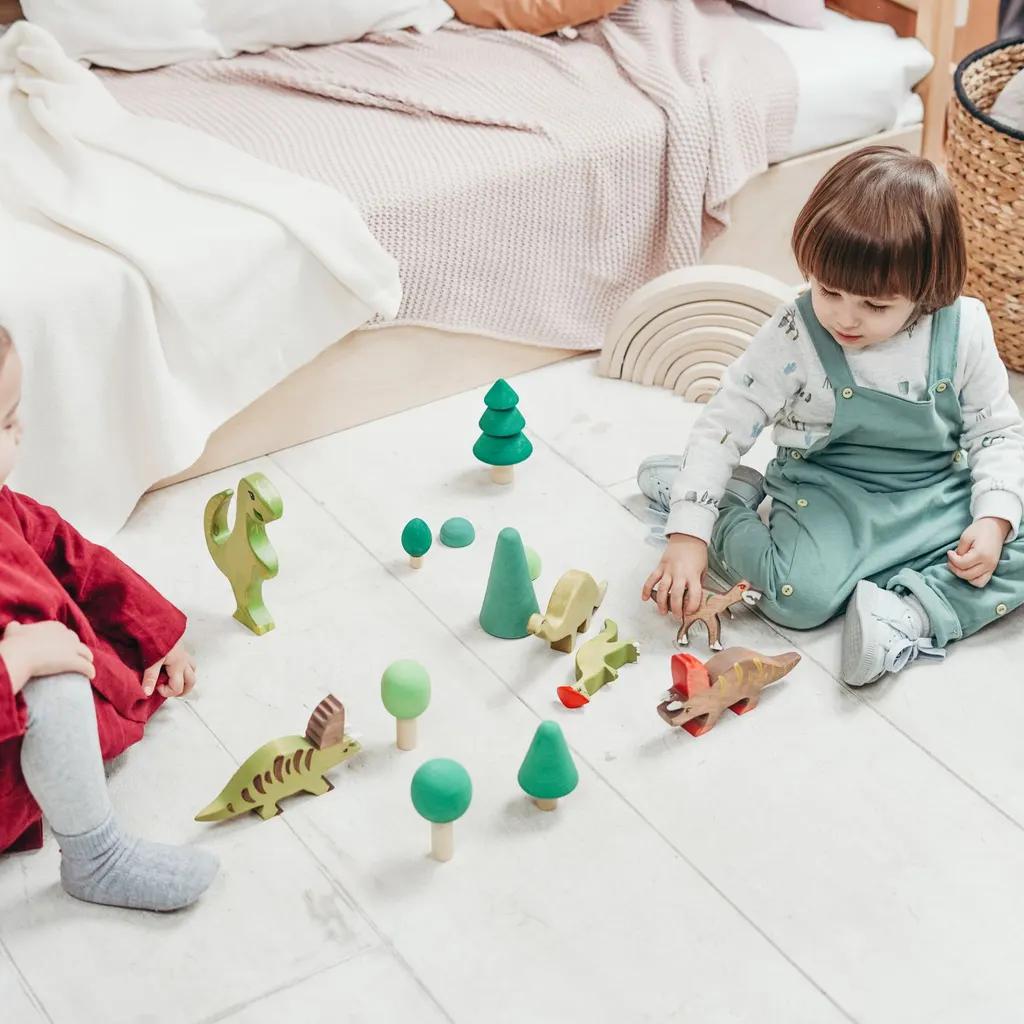 Two toddlers play with wooden toy dinosaurs on a white rug.